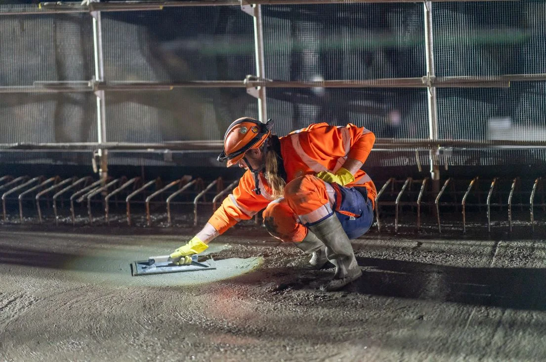 Ouvriere en combinaison orange qui lisse la chaussée de nuit