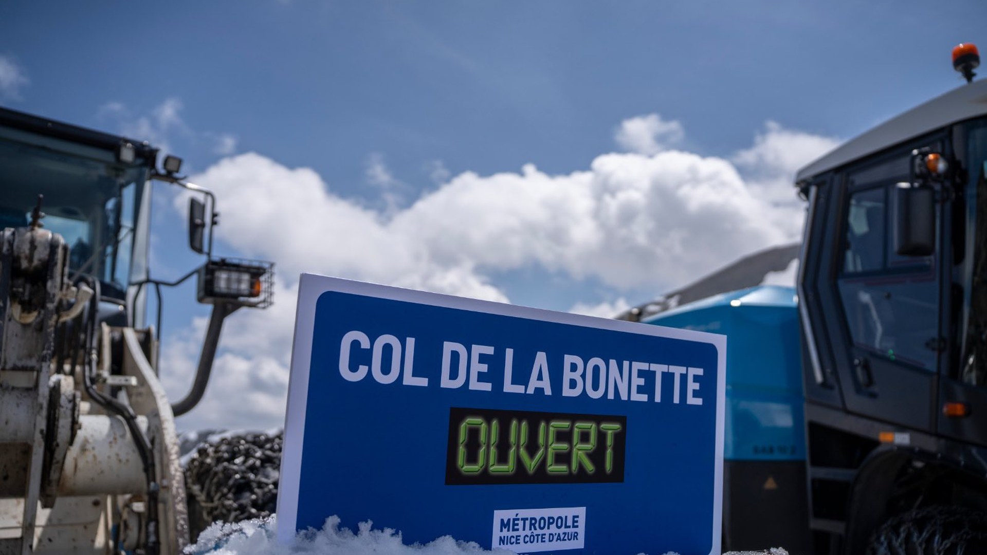 Panneau Col de la Bonette ouvert posé sur la neige, entre deux engins de déneigement
