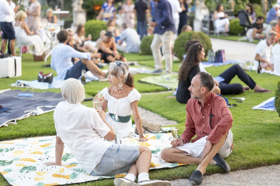 Groupe de spectateurs en pique-nique sur la pelouse de la Villa Ephrussi, coupes à la main