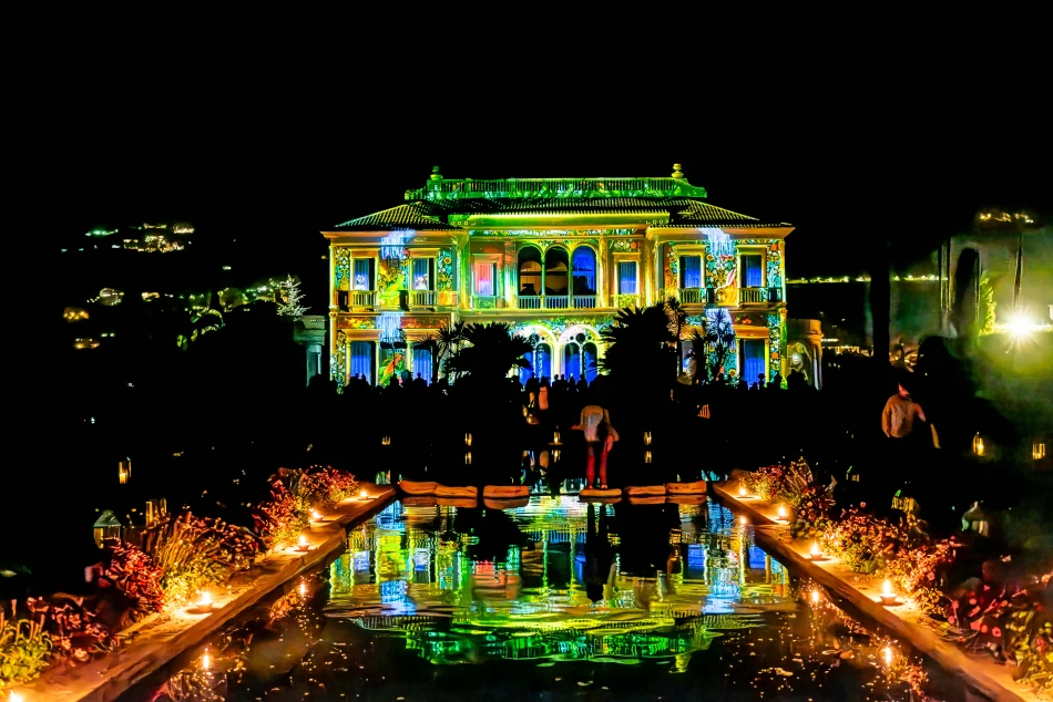Villa Ephrussi illuminée la nuit en projections vertes et jaunes, reflets dans le bassin