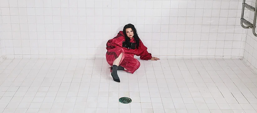 Lola Young en manteau rouge sur sol carrelé blanc