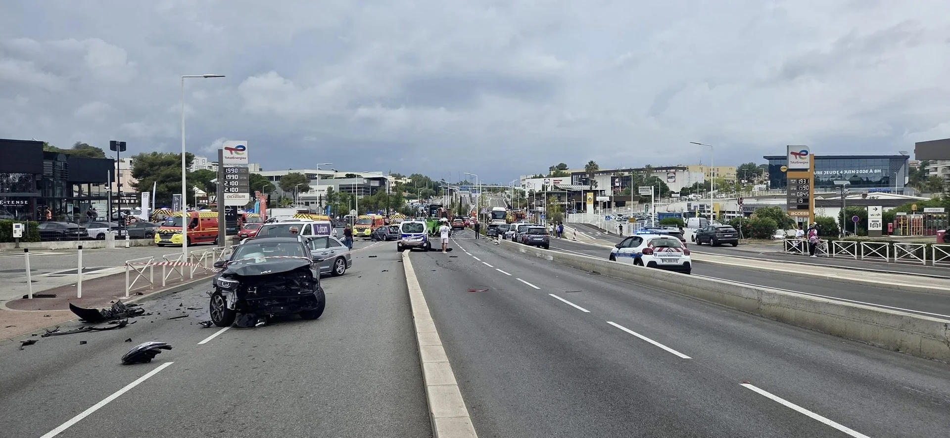 Vue de la route de Grasse après le carambolage : voiture à l'avant détruit, débris au sol, secours en arrière-plan, Antibes 2 juin 2026