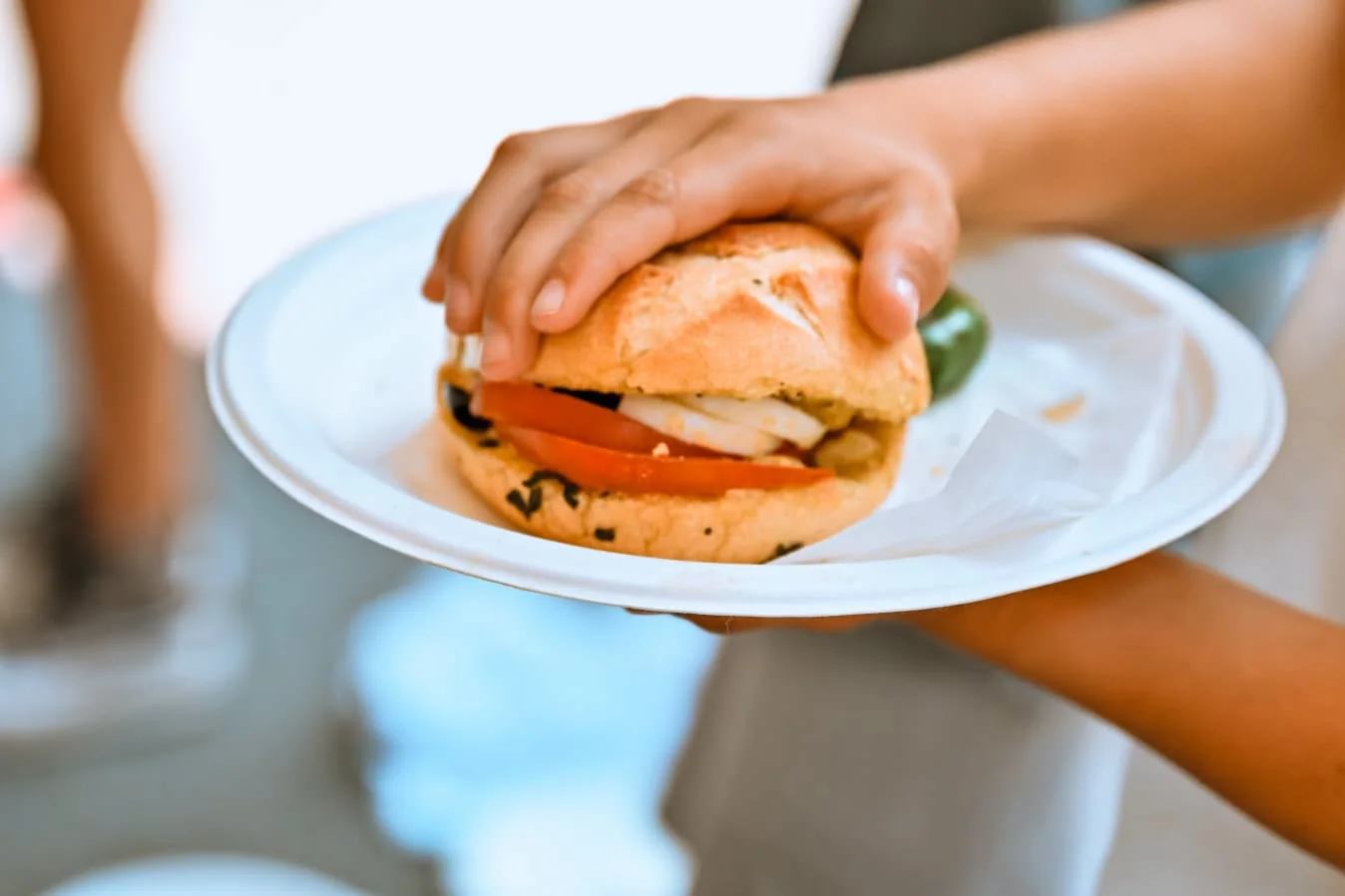 Mains d’un enfant tenant une assiette avec un pan bagnat au pain rond garni de tomate