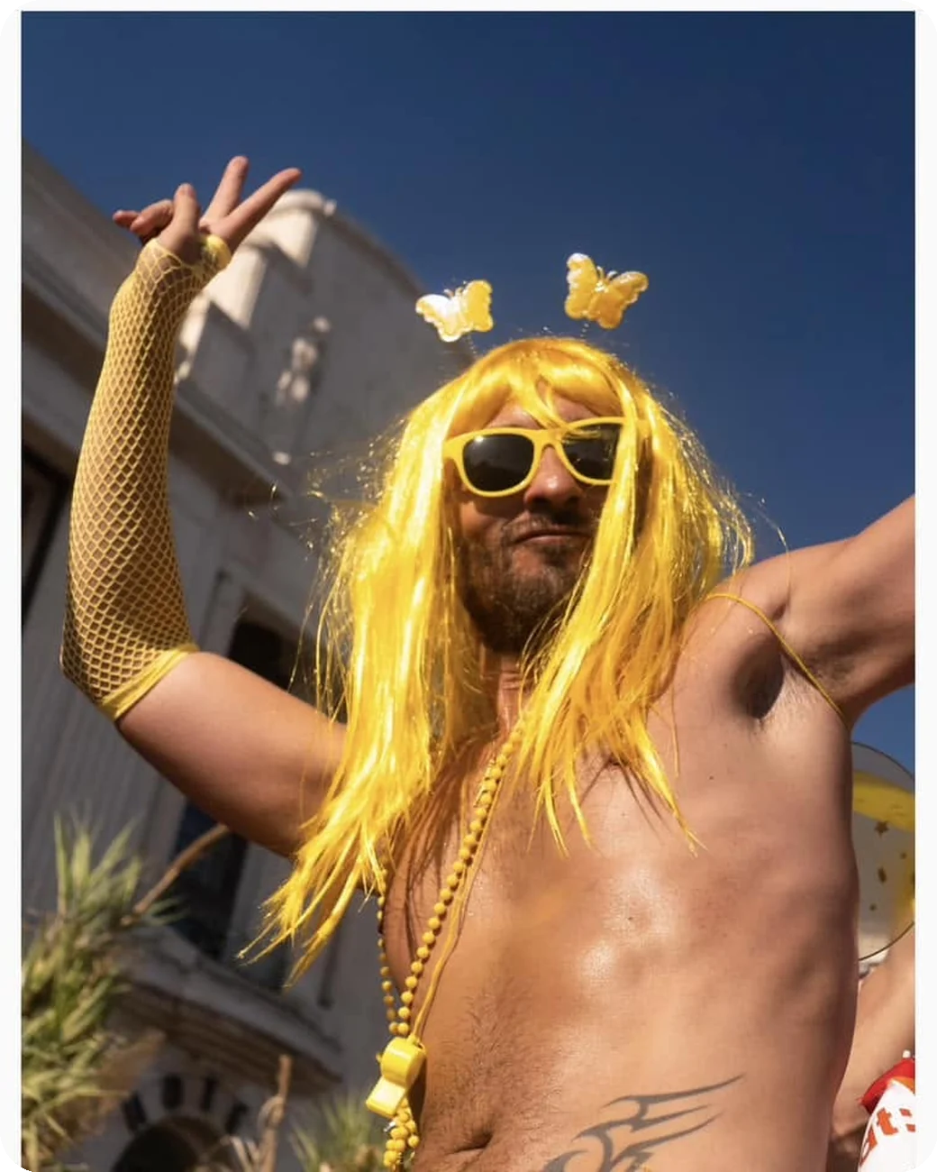 Participant en perruque jaune faisant le signe de la paix à la Pink Parade de Nice
