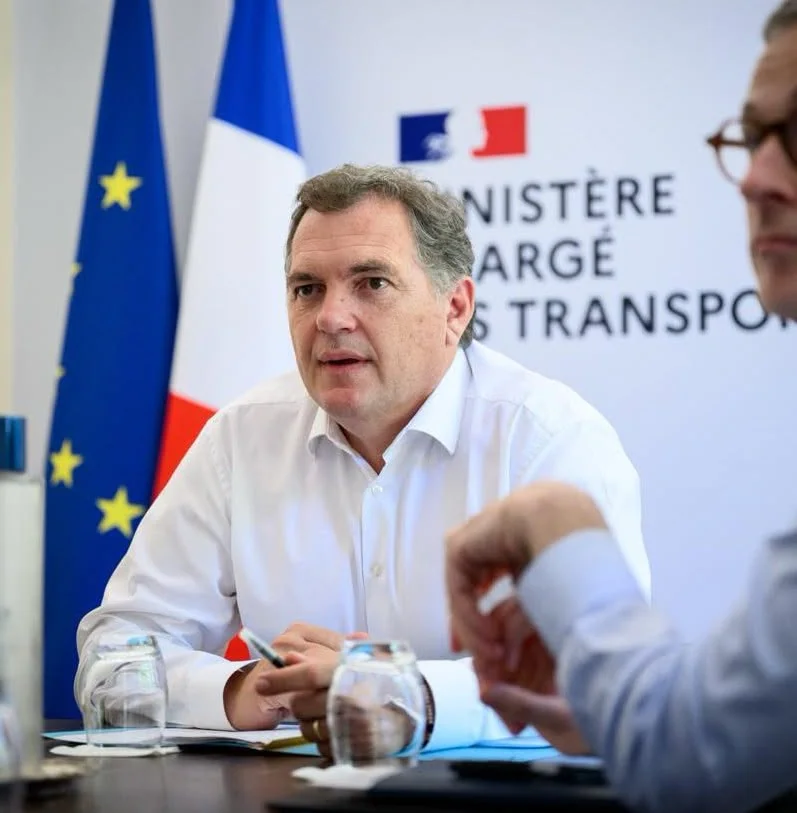 Philippe Tabarot, ministre des Transports, en chemise blanche devant le logo du ministère