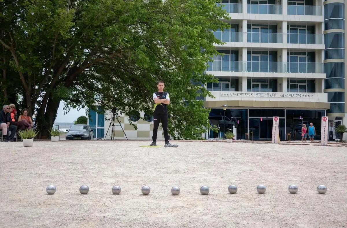 Tanguy Penin debout derrière une longue rangée de boules de pétanque alignées