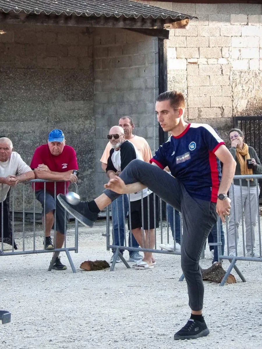 Tanguy Penin lève la jambe pour un tir freestyle de pétanque devant des spectateurs