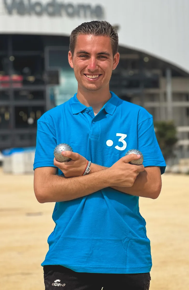Tanguy Penin souriant en polo bleu France 3, deux boules de pétanque en main