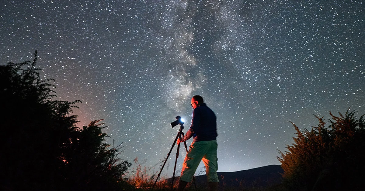 Un photographe sous la Voie lactée, appareil sur trépied, dans la nuit noire