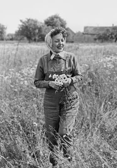 Édith Piaf en salopette dans un champ, un bouquet de fleurs à la main