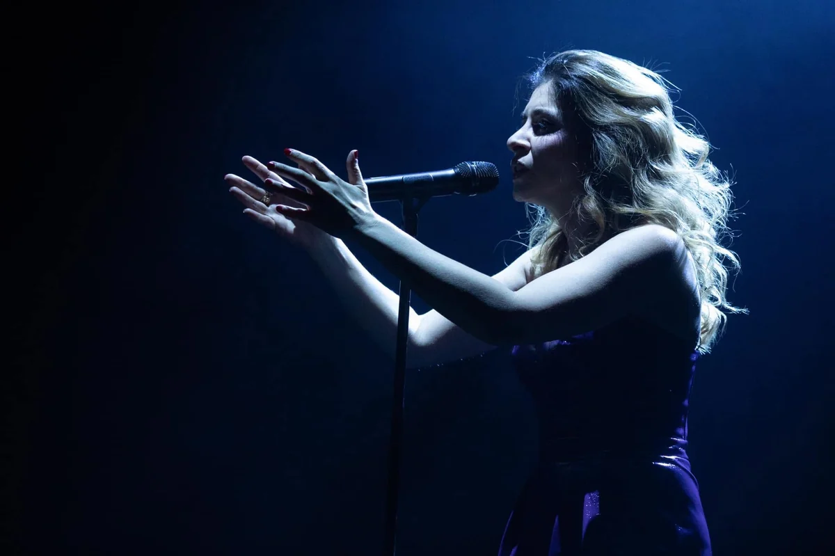 Julie Zenatti chante sur scène, micro sur pied, sous les lumières bleues