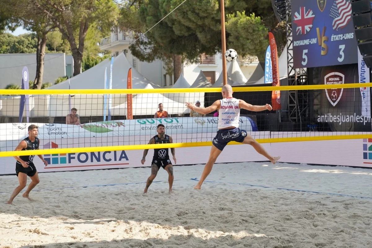 Joueur de footvolley britannique en grand écart suspendu au-dessus du sable, jambes écartées