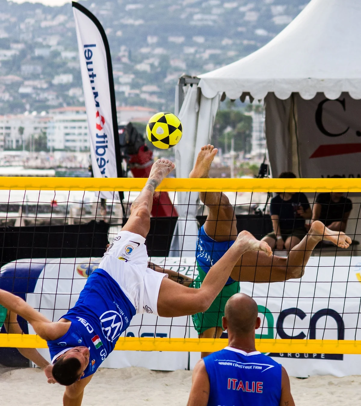 Joueur de footvolley en retourné acrobatique au-dessus du filet, pieds en l’air