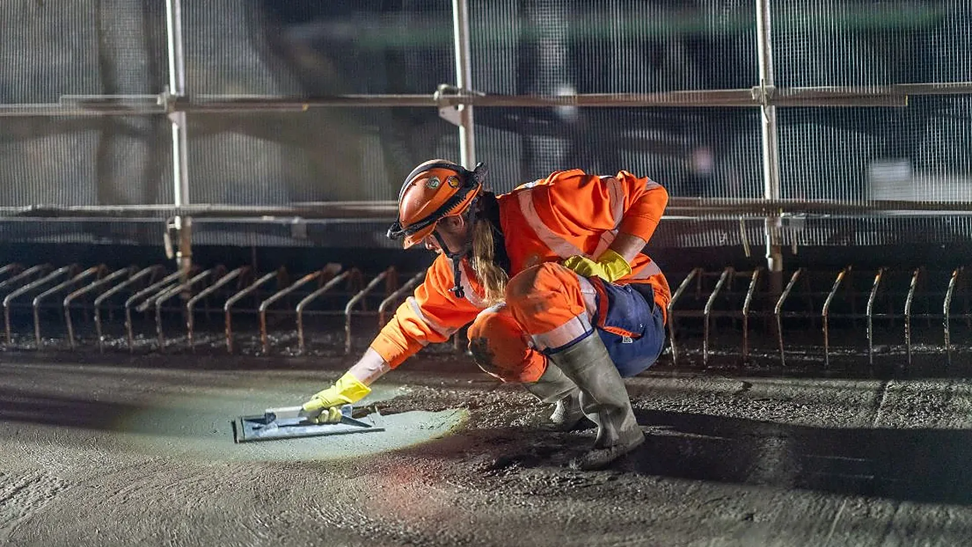 Ouvrière en combinaison orange lissant la chaussée de nuit
