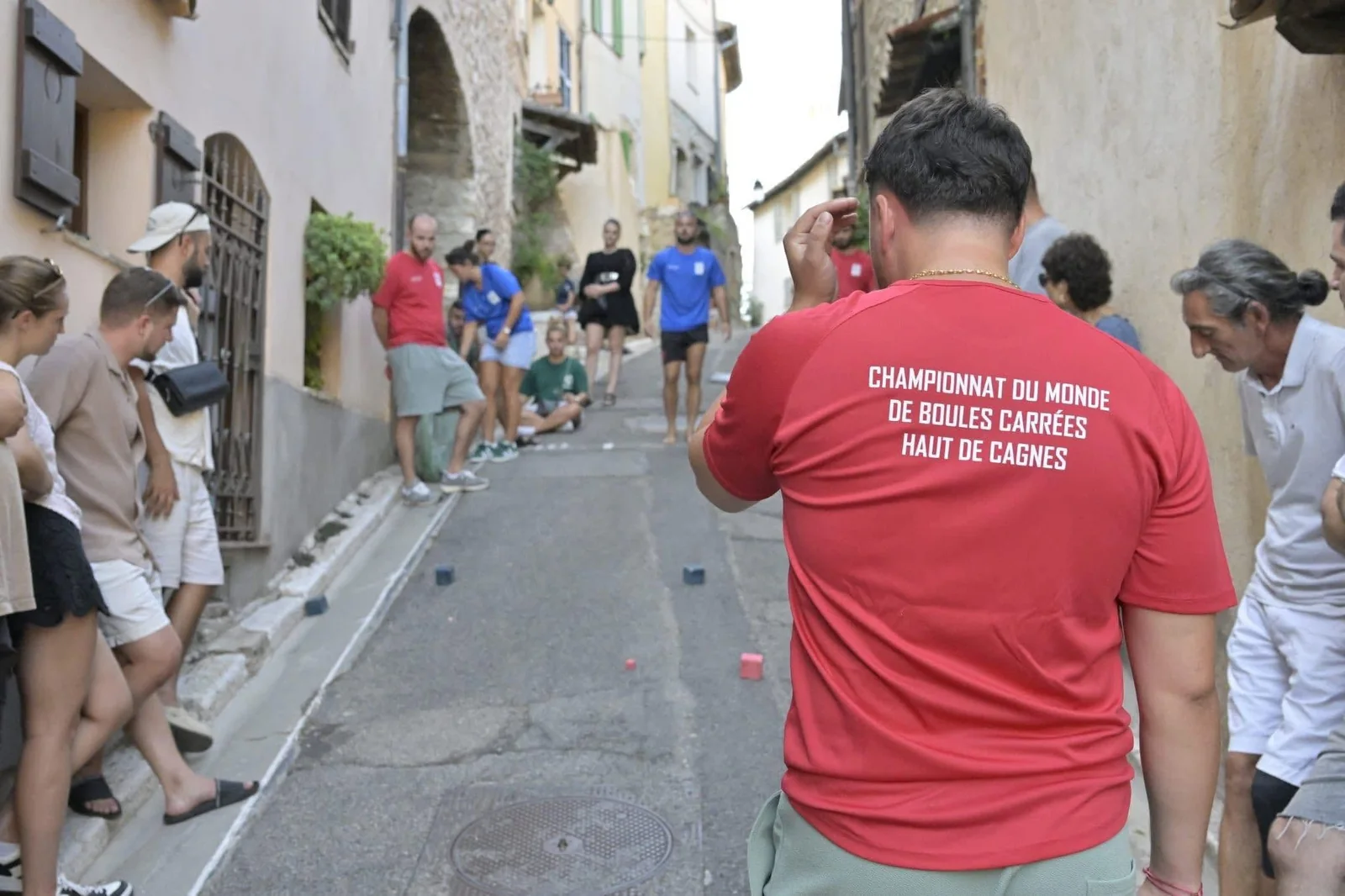 Un joueur de dos en maillot rouge Championnat du monde de boules carrées Haut de Cagnes, dans une ruelle en pente
