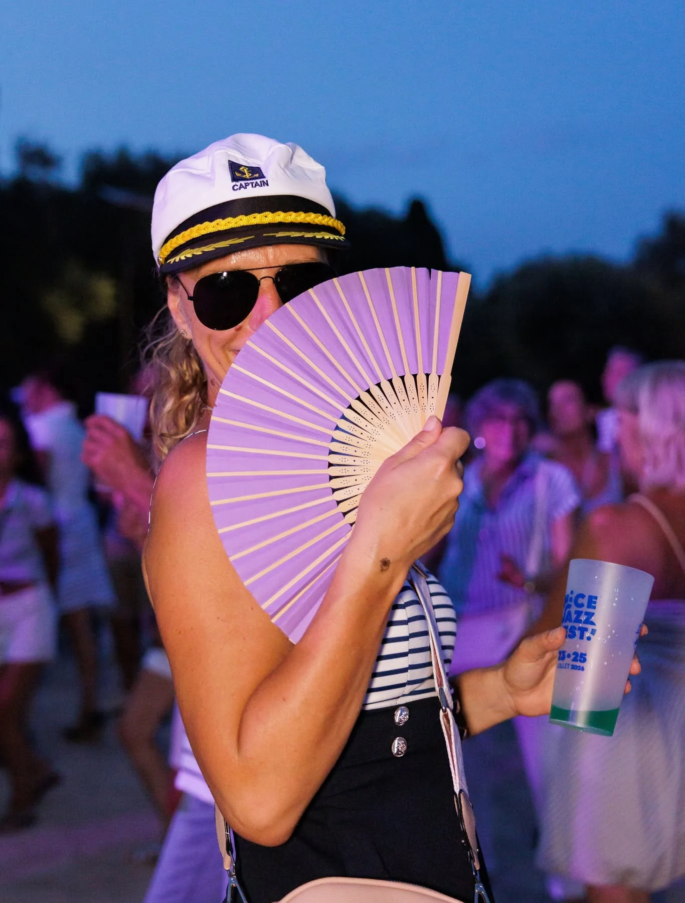 Une festivalière en casquette de capitaine avec un éventail