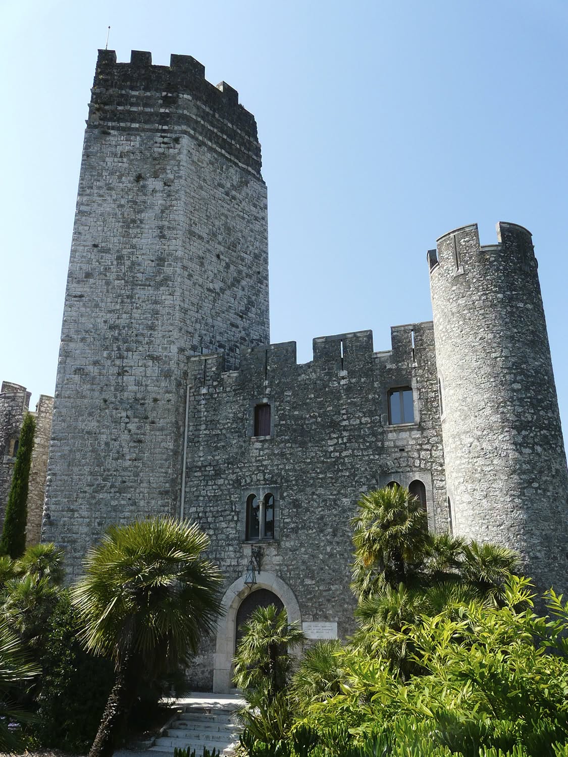 Le donjon carré et une tour ronde crénelée de la forteresse médiévale de Villeneuve-Loubet, entourés de palmiers