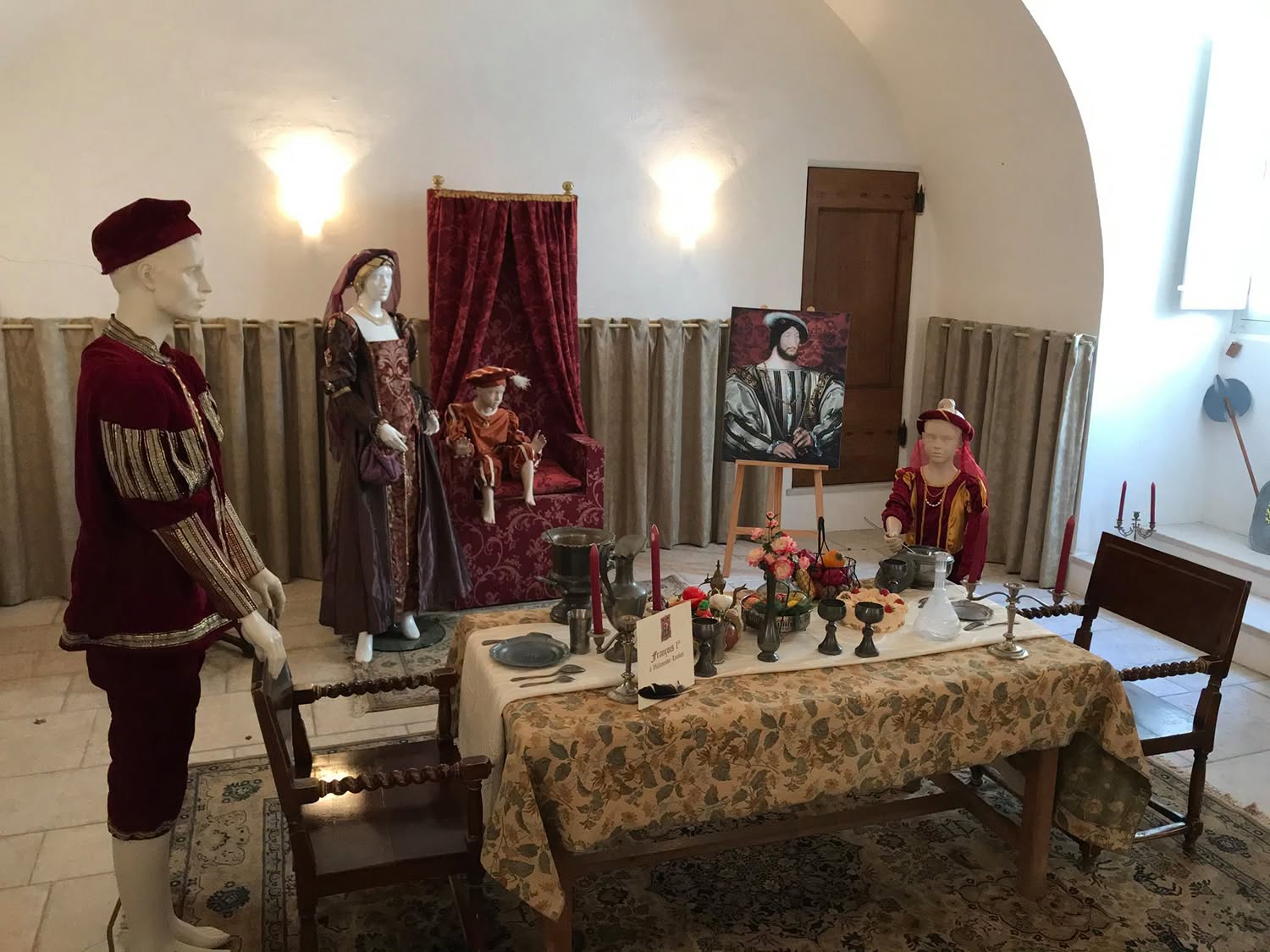 Salle aménagée de la forteresse de Villeneuve-Loubet : table dressée, trône et mannequins en costumes Renaissance devant un portrait de François Ier