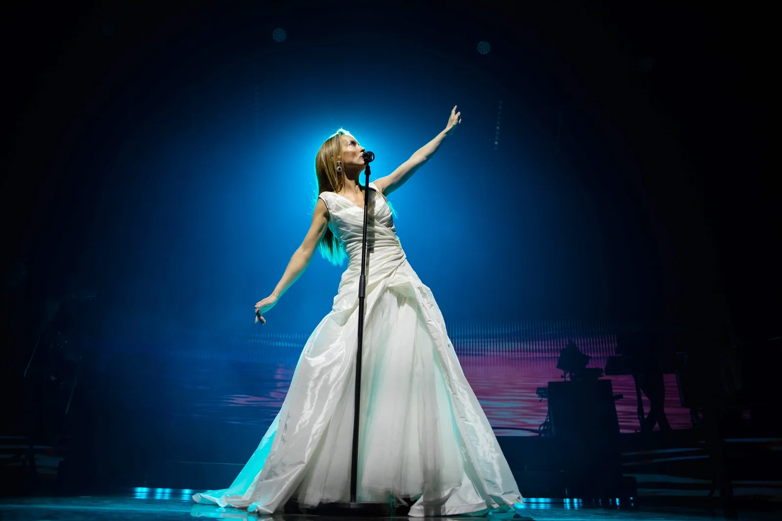 Une chanteuse en longue robe blanche, bras tendu vers le haut, sous une lumière bleue