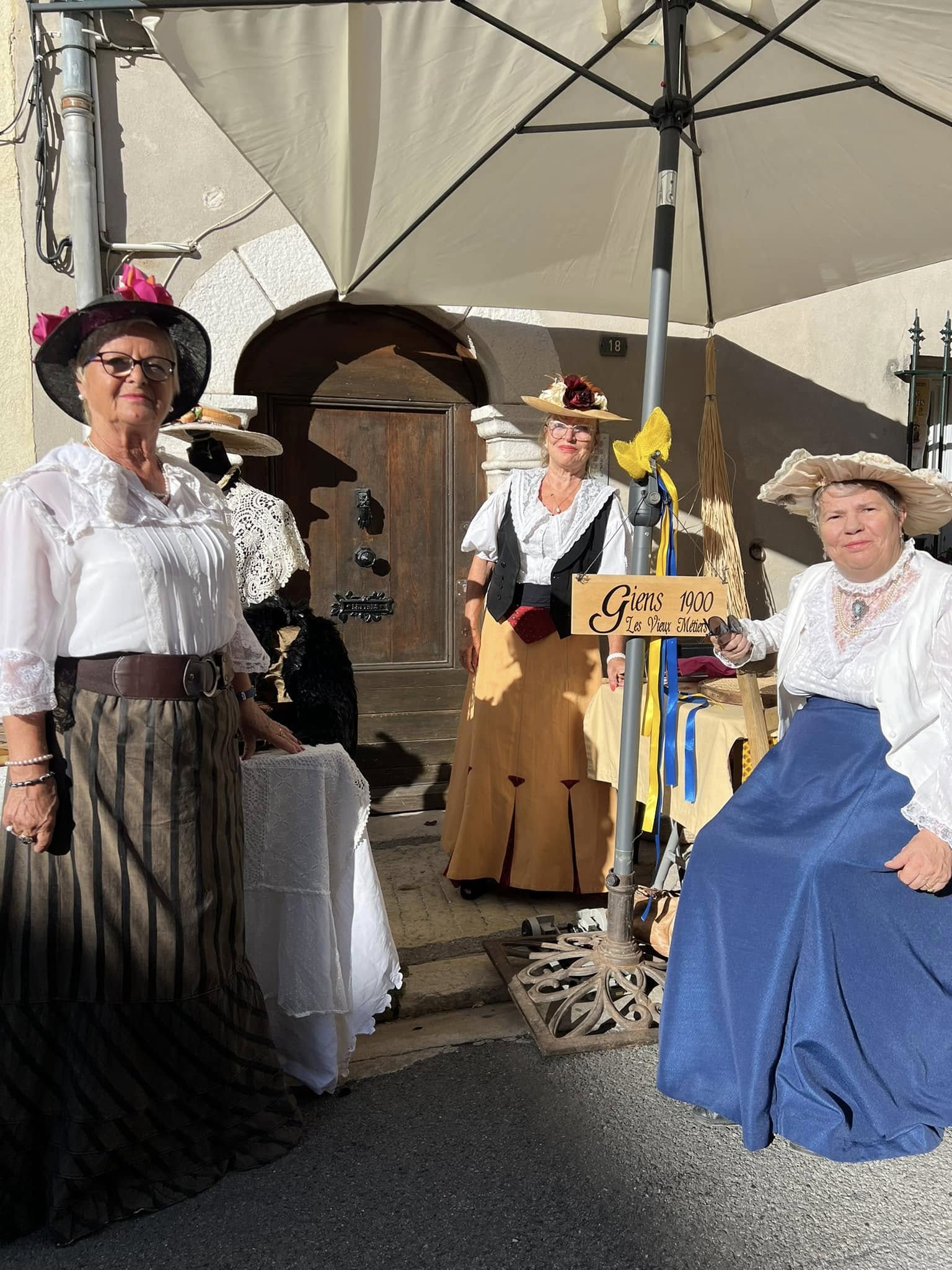 Trois femmes en costumes anciens, chapeaux fleuris et jupes longues, dans une ruelle de La Colle-sur-Loup pendant La Colle Autrefois