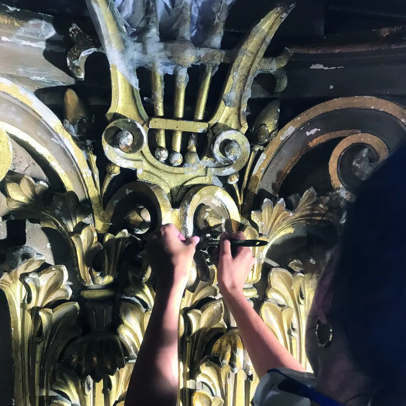 Une restauratrice travaille au pinceau sur un chapiteau doré à la lyre, dans la salle de l'Opéra de Nice