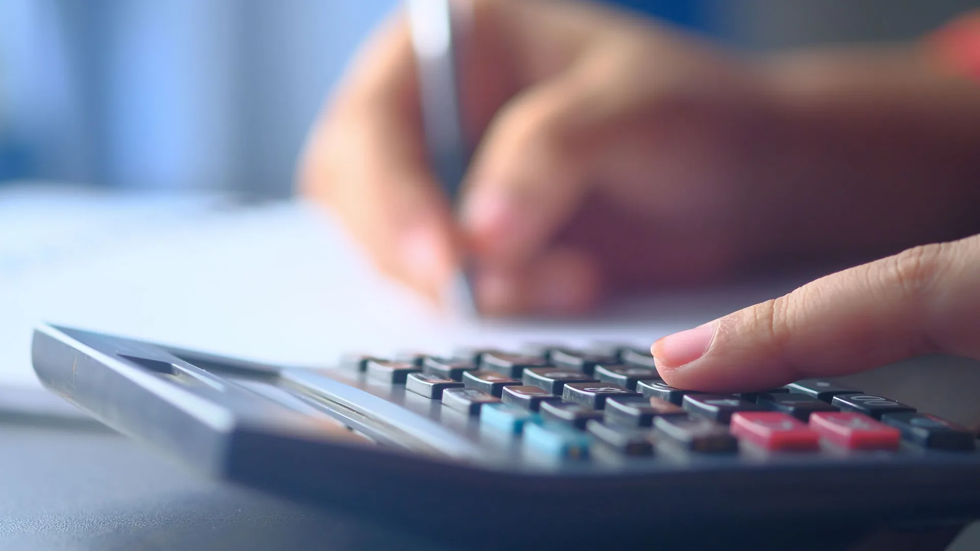 Une main tape sur une calculatrice à côté d'un bloc-notes et d'un stylo