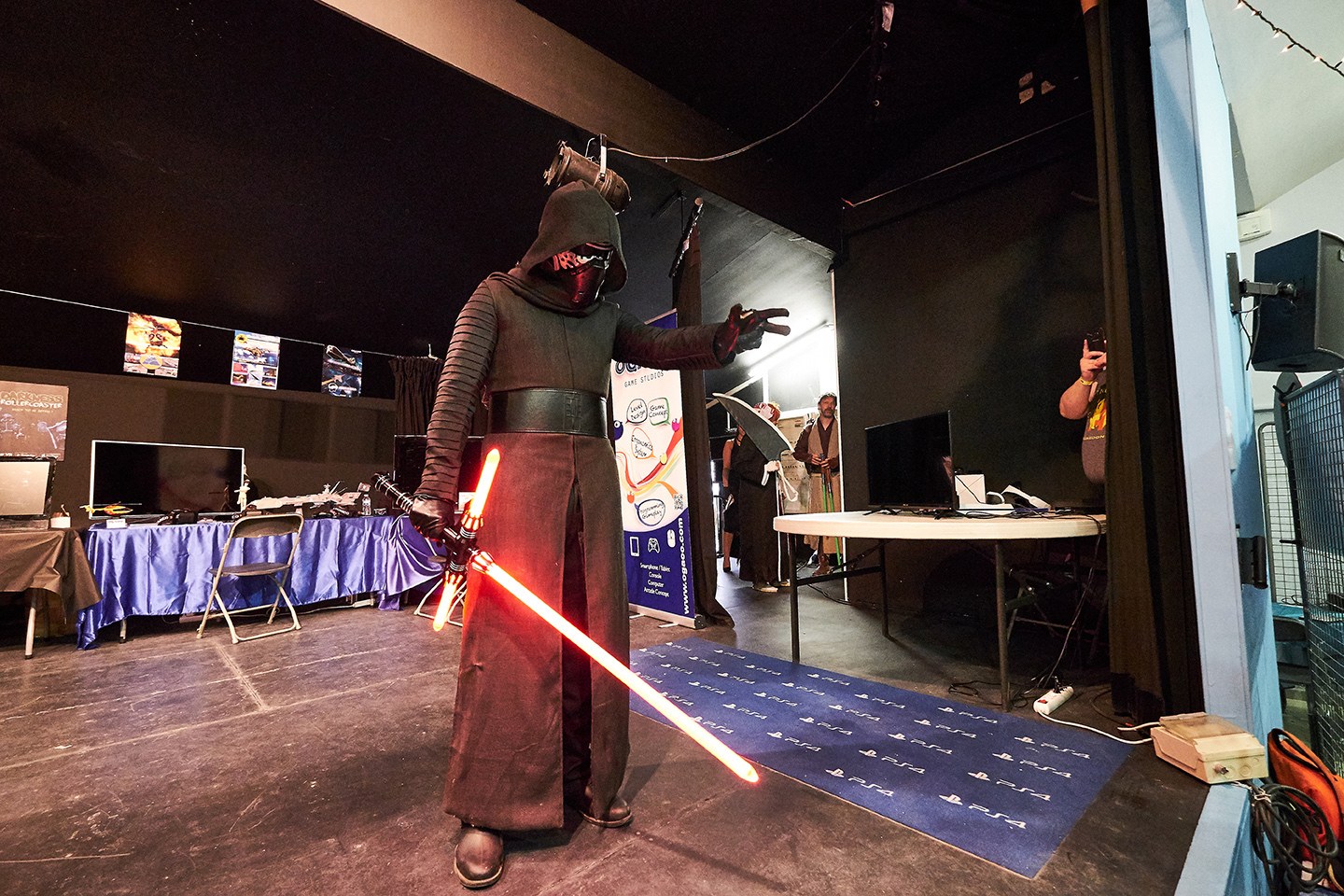 Cosplayeur en tenue noire avec un sabre laser rouge sur la scène de la salle Léo Lagrange