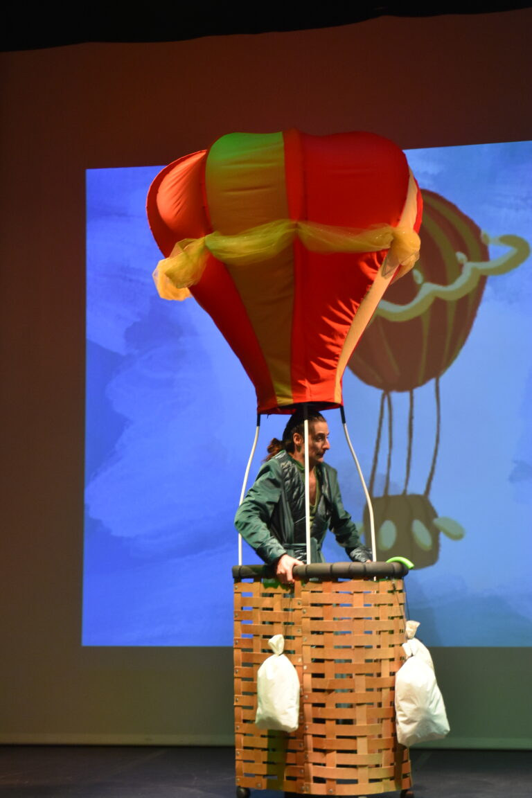 Le Magicien d'Oz dans sa montgolfière rouge et jaune devant un décor de ciel dessiné