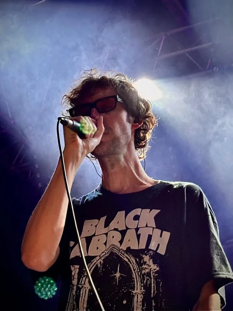 Le chanteur de Pony Pony Run Run au micro, lunettes noires, sous les projecteurs