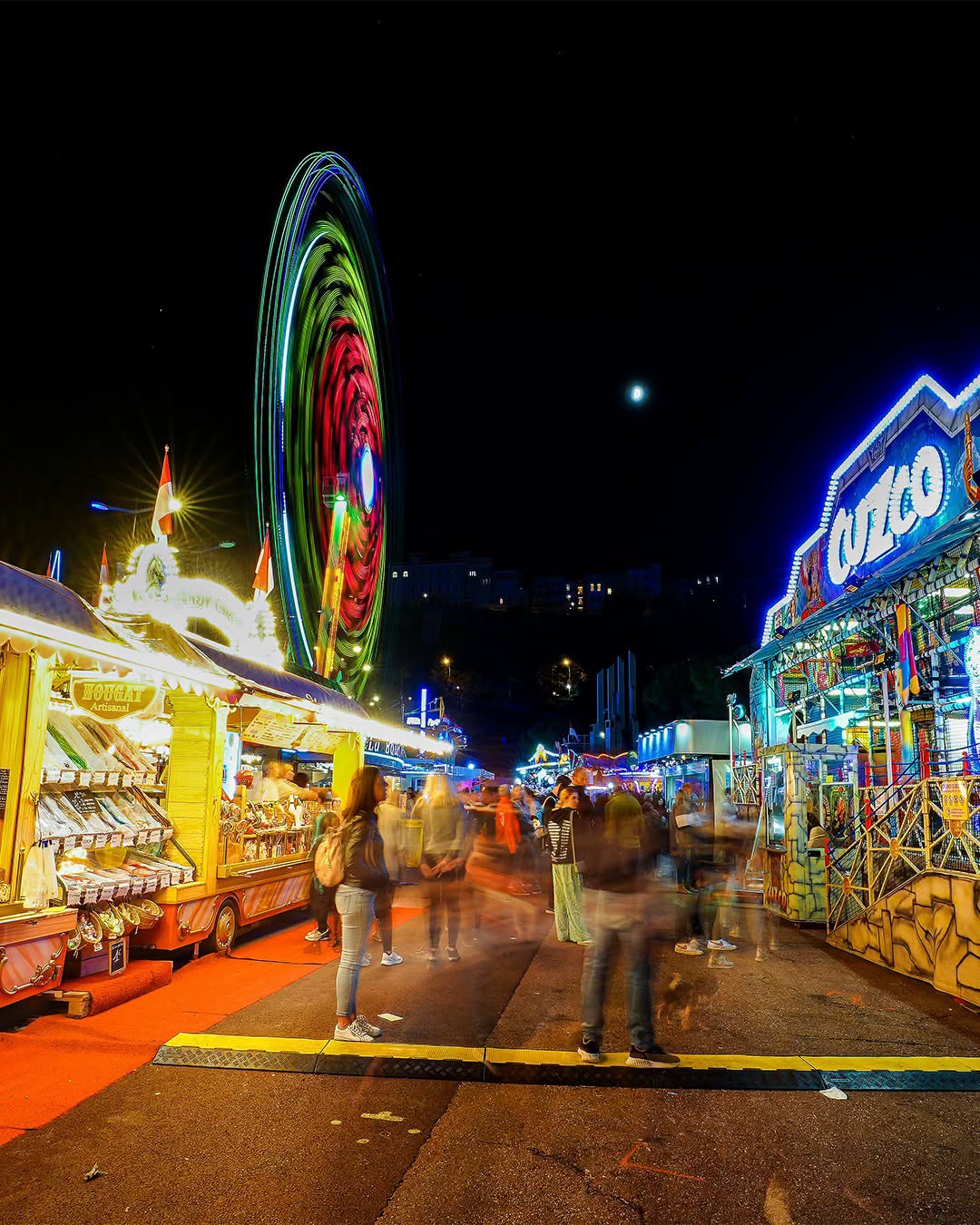La grande roue lumineuse en pose longue et les stands de la Foire Attractions sur le port Hercule de Monaco, de nuit